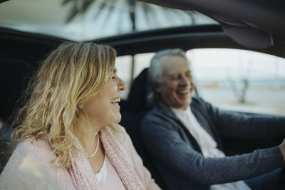 Mature blond woman laughing by man sitting in car