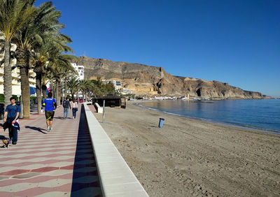 People walking on beach against clear blue sky