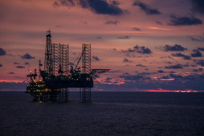 Cranes at sea against sky during sunset