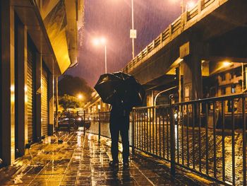 Rear view of man with umbrella on footpath at night