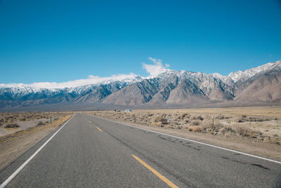 Road by snowcapped mountains against clear blue sky