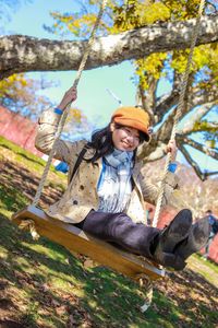 Cheerful young woman sitting on swing at playground