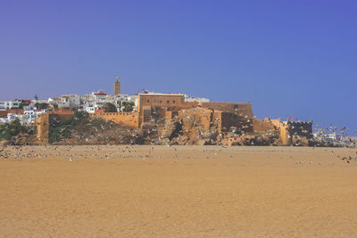 Buildings by sea against clear blue sky