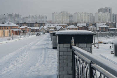 Snow covered houses by buildings in city against sky