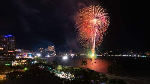 Firework display over illuminated city against sky at night