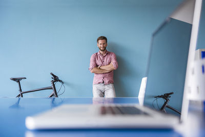 Portrait of smiling man and laptop in break room of modern office