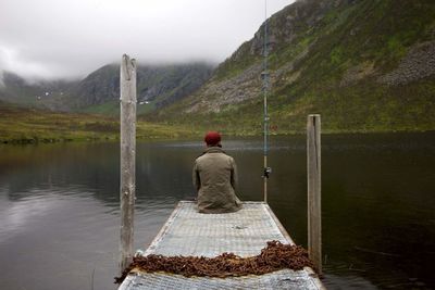 Rear view of man sitting on pier over lake