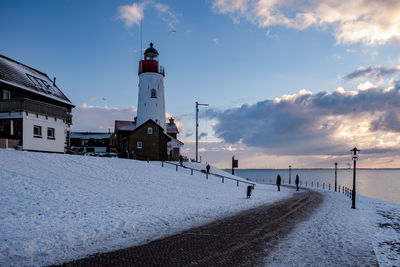 Lighthouse amidst buildings against sky during winter