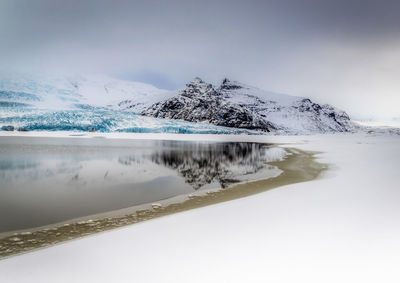 Scenic view of lake by snowcapped mountain against sky