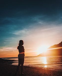 Silhouette woman standing at beach against sky during sunset