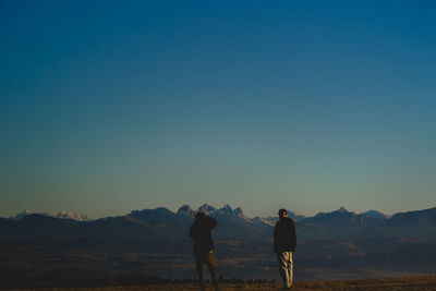 Silhouette men standing on mountain against clear sky