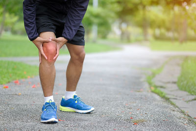 Low section of man touching aching knee while standing on footpath