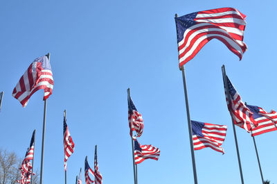 Low angle view of american flags waving against clear blue sky