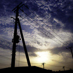 Low angle view of electricity pylon against cloudy sky