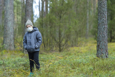 Girl wearing hooded jacket and mask standing in forest