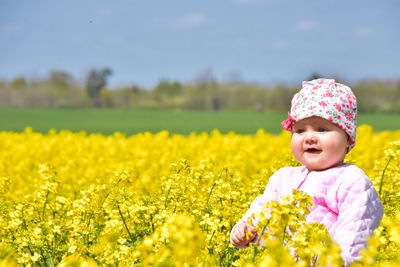 One happy 9 month old baby girl in rapeseed blooming field