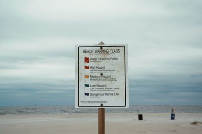 Information sign on beach against sky