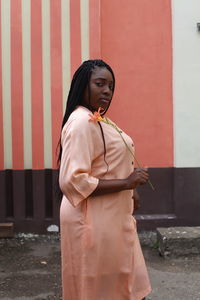 Portrait of young woman holding flower while standing against wall