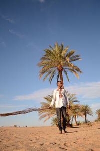 Man looking away standing at beach holding palm leaf against sky