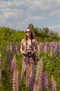 Beautiful young woman in the field of lupins with photo camera
