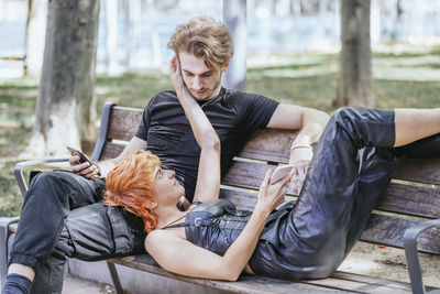 Young couple with smart phone on bench at park