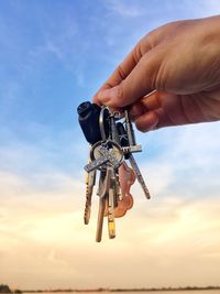 Cropped hand holding keys against sky 