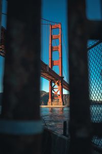 Low angle view of golden gate bridge over bay seen through fence