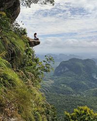 Woman sitting on mountain against cloudy sky