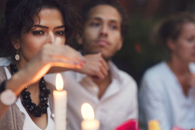 Woman covering candle while sitting with friends at garden party