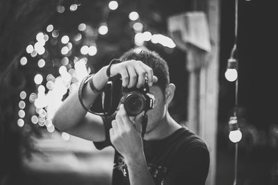 Portrait of young man photographing illuminated camera