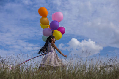 Low angle view of cute girl holding balloons while running on land against sky