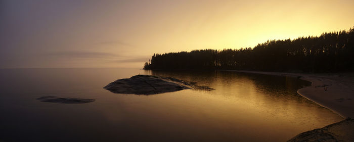 Scenic view of rocks by trees against sky during sunset