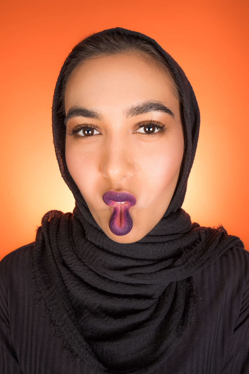 PORTRAIT OF YOUNG WOMAN AGAINST ORANGE BACKGROUND