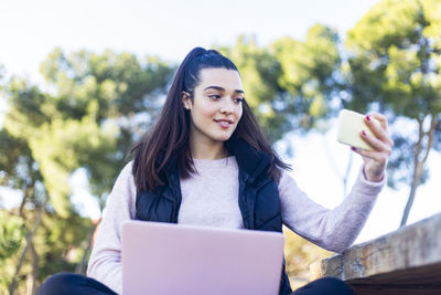 Low angle view of woman taking selfie with smart phone while sitting in park