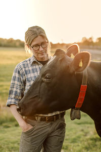 Female farmer standing by cow at field during sunset