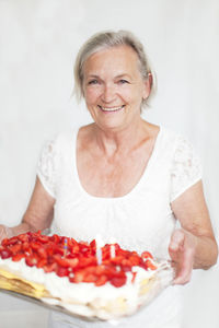 Senior woman holding strawberry cake, studio shot
