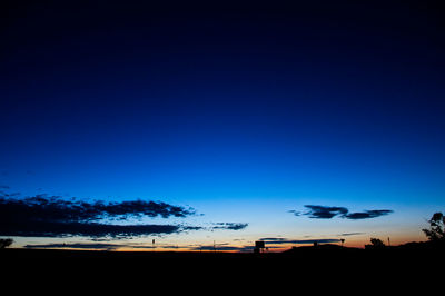 Silhouette trees on landscape against blue sky