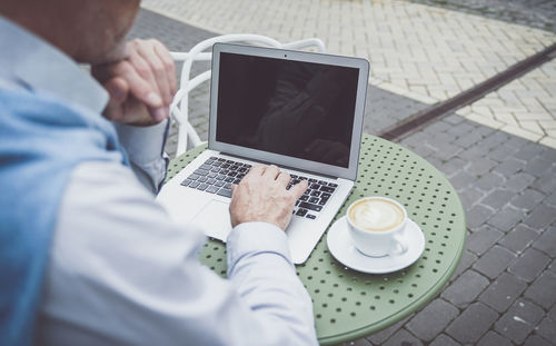 Midsection of senior man using laptop while sitting at cafe