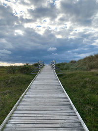 Wooden boardwalk leading towards landscape against sky