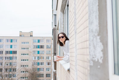 Portrait of young woman standing against window