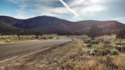 Empty country road leading towards mountain against sky