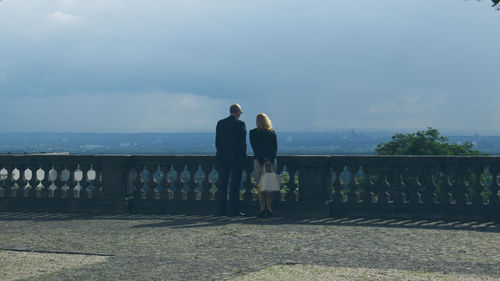 Rear view of couple standing by railing against sky