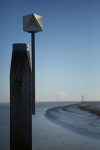 Close-up of wooden post by sea against clear blue sky