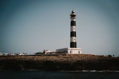 Lighthouse by sea against clear sky