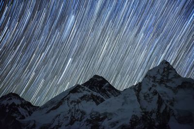 Low angle view of snow covered mountains against star trails