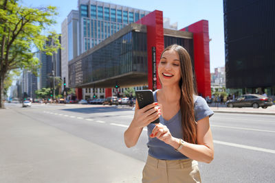 Young woman using mobile phone while standing against buildings in city