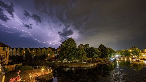 Panoramic shot of illuminated trees by river against sky at night