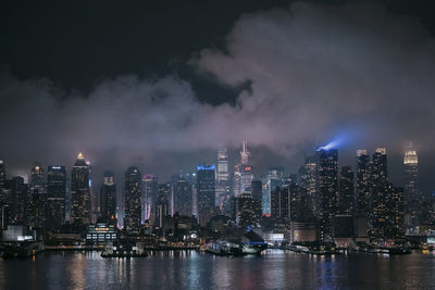 Illuminated city by river against sky at night