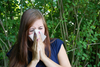 Sick woman wiping her nose against plants