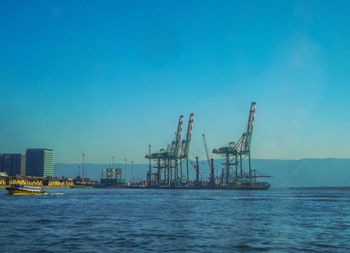 Cranes in sea against clear blue sky